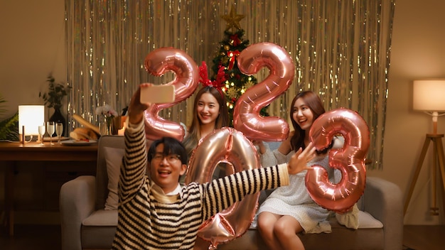 New Year party concept Group of friends holds balloon air pink gold number 2023 and taking selfie