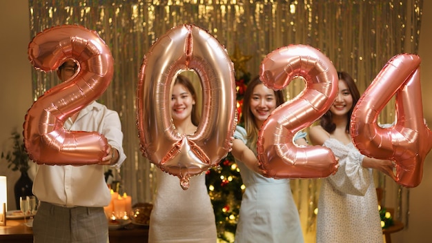 New Year party concept Group of friends holds balloon air pink gold number 2024 in new year party