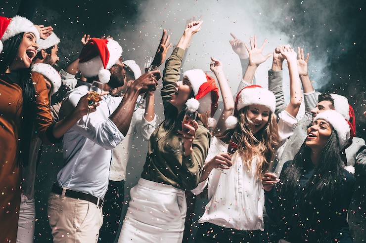 Photo new year party. group of beautiful young people in santa hats throwing colorful confetti and looking happy