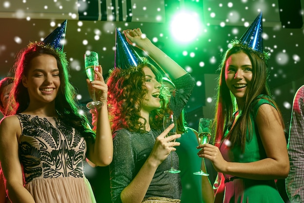 new year party, holidays, celebration, nightlife and people concept - smiling friends with glasses of non-alcoholic champagne in club and snow effect