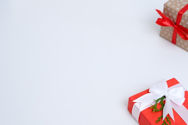 Regali di capodanno in scatole regalo avvolti in carta punteggiata artigianale e legati con un fiocco di nastro rosso due pacchetti decorati con ramoscello di abete su sfondo bianco con copyspace