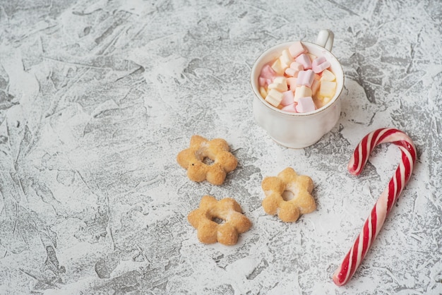 Новогодняя или рождественская композиция чашка с зефиром с конфетами и печеньем на ярком текстурном фоне