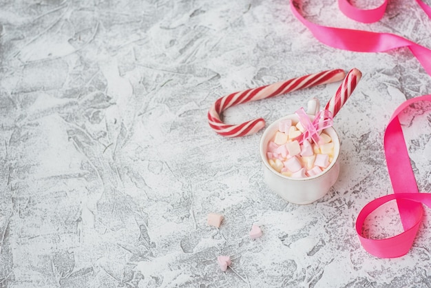 New Year's or Christmas composition cup with marshmelow with candy among New Year's, shiny toys and pink ribbon on a bright textural background. Flat lay, layout