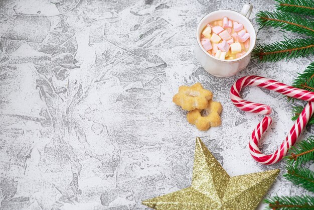 New Year's or Christmas composition of spruce green branches, New Year's star, cup with marshmallows, cookies and Christmas lollipops on a bright textural background. Flat lay, layout, copy space
