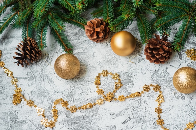 トウヒの緑の枝、松ぼっくり、正月、光沢のある金色、明るいテクスチャの背景のおもちゃの新年またはクリスマスの構成。フラットレイ、レイアウト、フレーム、テキストの場所、コピースペース