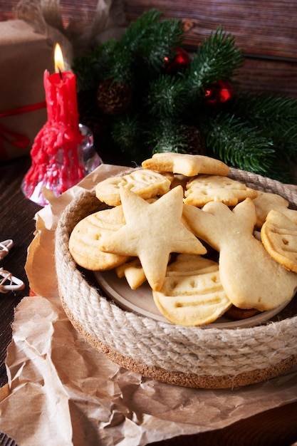 New Year's cookies in a handmade plate lie on the table next to the branch of the Christmas tree and a burning candle