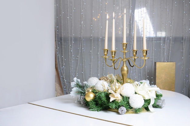 New Year's decorations and a golden candlestick with burning candles stand on the surface of a white grand piano