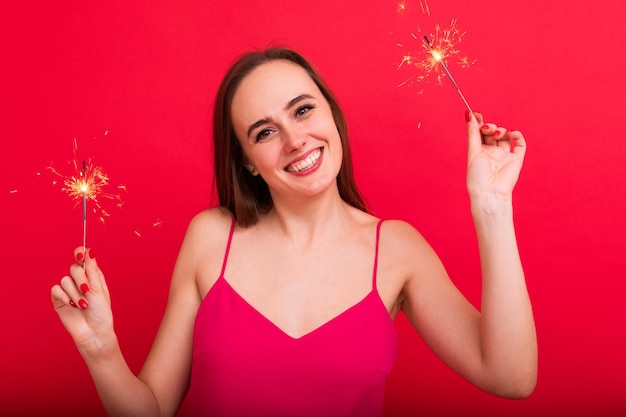 New Year's Eve party Portrait of a young woman in a pink dress holding sparklers in a good mood