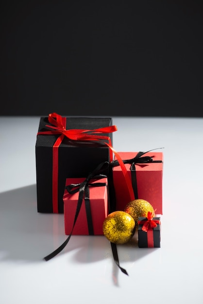 Новогодние подарки красно-черного цвета с игрушками на белом столе и темном фоне