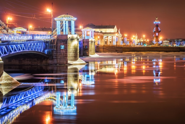 The New Year's Palace Bridge in St. Petersburg and the Rostral Columns are reflected in the river Neva in the light of night lights