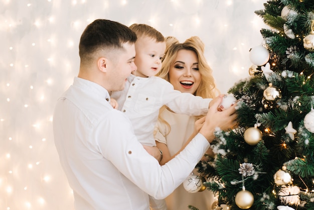 New year's portrait of a beautiful young family. Attractive parents and a little son decorate a Christmas tree