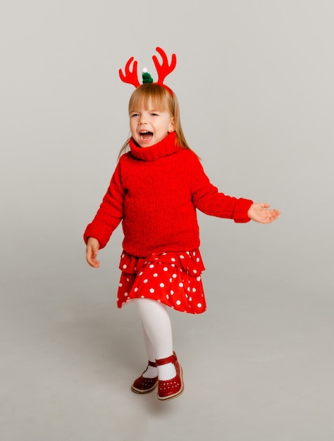 New Year's portrait of a little girl in a deer frame and a red sweater on a white background.