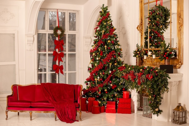 New Year's red and gold interior with a large spruce tree, a red sofa, a fireplace and red boxes