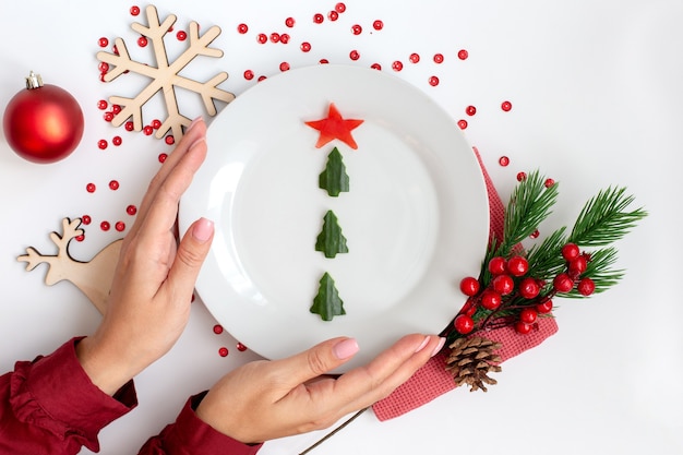 New Year's table decor. Female hands hold a plate with a cucumber snack in the form of a Christmas tree