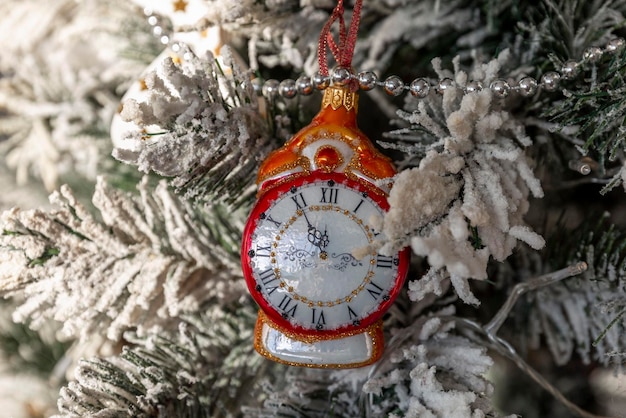 New Year's toy clock on a decorated Christmas tree Traditions and holidays Closeup