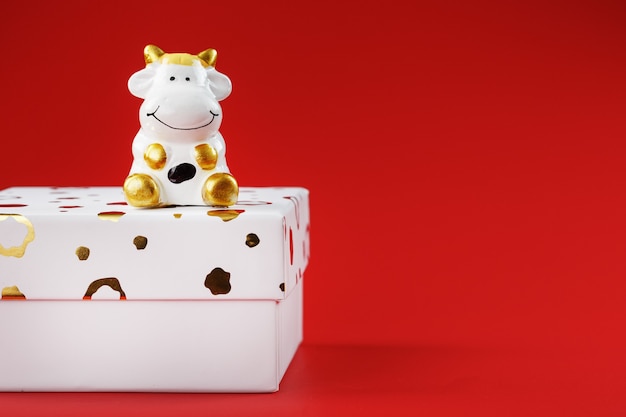 赤い背景の上の贈り物と箱の上の牛の新年のおもちゃ