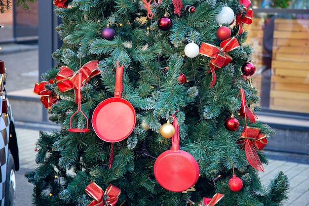 Albero di capodanno sulla strada della città, decorato con utensili da cucina. decorazioni natalizie da una padella e una frusta. design insolito dell'albero di natale