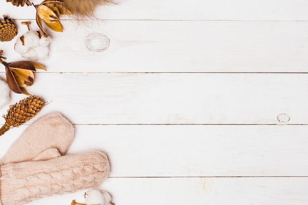 New year white wooden background for copy space. Beige knitted mittens, fur pompom, winter floristry attributes on the table. Winter cozy, Flat lay