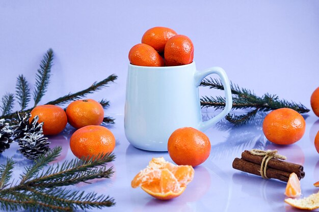 Фото Новый год натюрморт с мандаринками мандаринки в голубой чашке на голубом фоне рядом с мандаринами и еловыми ветвями отражение от предметов