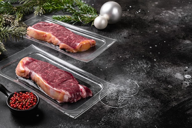 New york beef gemarmerd vlees vacuümverpakte steak in kerststijl, op zwarte donkere stenen tafelachtergrond, met kopieerruimte voor tekst