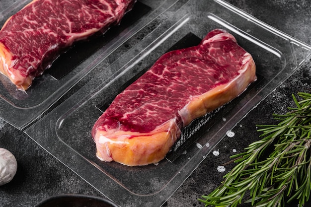 New York beef steak cut in plastic pack set, on black dark stone table background