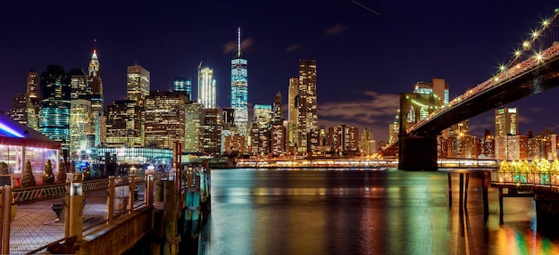 New York City Brooklyn Bridge en Manhattan skyline met wolkenkrabbers over Hudson River verlicht met lichten in de schemering na zonsondergang.