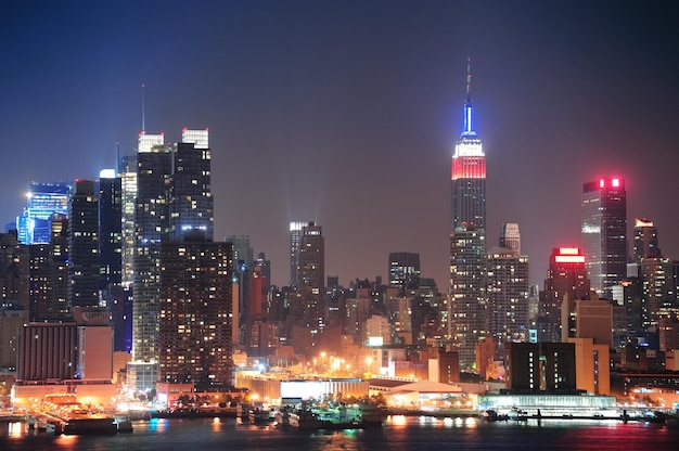 Горизонт центра города нью-йорка манхэттена ночью с небоскребами, освещенными над рекой гудзон с отражениями.