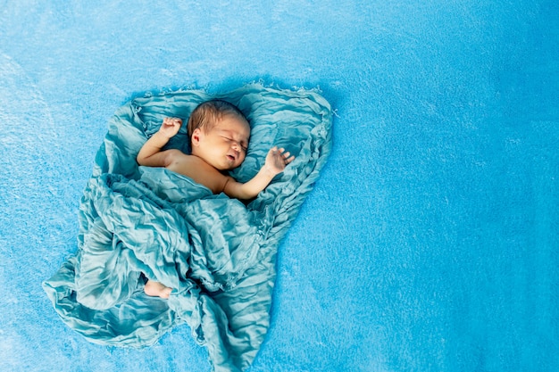 Newborn 14 day old baby boy lying on his back relaxing under a blue wrap cloth