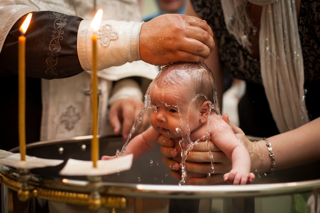 写真 聖水で生まれたばかりの赤ちゃんの洗礼。赤ちゃんは母親の手を繋いでいます。幼児は水を浴びます。フォントの洗礼