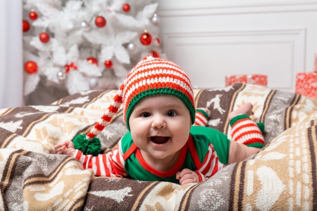 Newborn baby boy dressed in gnome costume lying on white fur carpet among christmas decorations