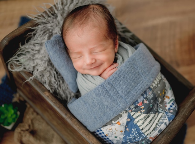 Newborn baby boy sleeping under handmade blanket in tiny wooden bed and smiling. Infant child kid napping portrait