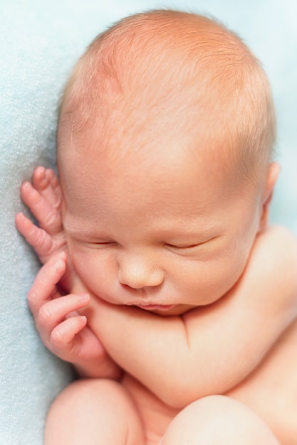 水色の背景で寝ている生まれたばかりの赤ちゃんの男の子。肖像画のクローズアップ