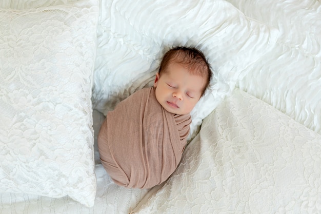 生まれたばかりの赤ちゃんの男の子は白いベッドで眠る