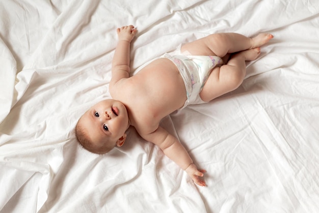 Newborn baby in a diaper is lying on his back on a white sheet. products for children, toy. concept of a happy childhood and motherhood. child care. space for text. High quality photo