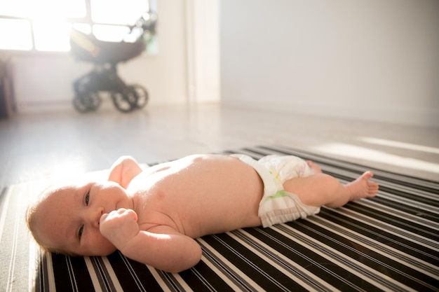 A newborn baby in a diaper lying on a bed and holding his fist near his face