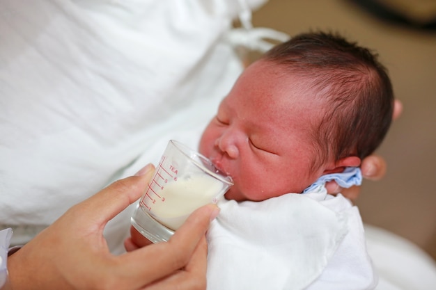 Newborn Baby drinking milk from glass cup.