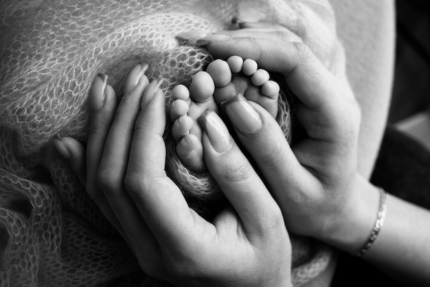 写真 mother39sの手で生まれたばかりの赤ちゃんの足ママと彼女の子供親は彼の手で生まれたばかりの子供の足を持っています幸せな家族と母性の概念プロのマクロクローズアップ白黒