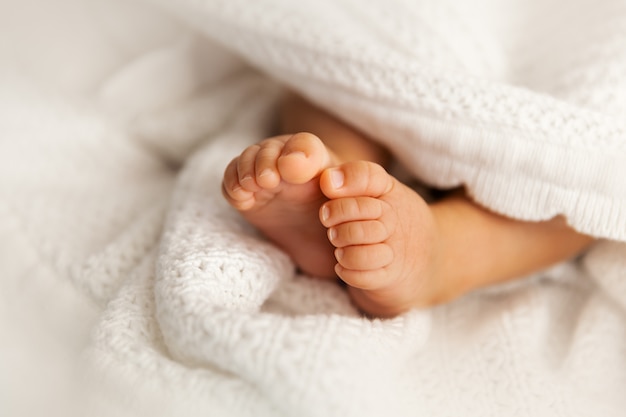 白い毛布の下で生まれたばかりの赤ちゃんの足、幼児の裸足のクローズアップ