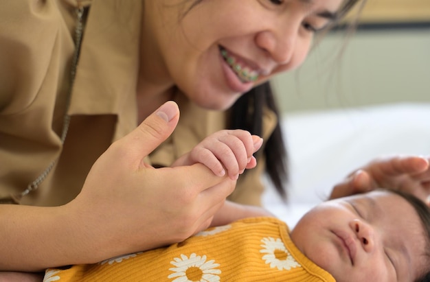 Newborn baby girl holding mother hand Smiling mom and child on white bed