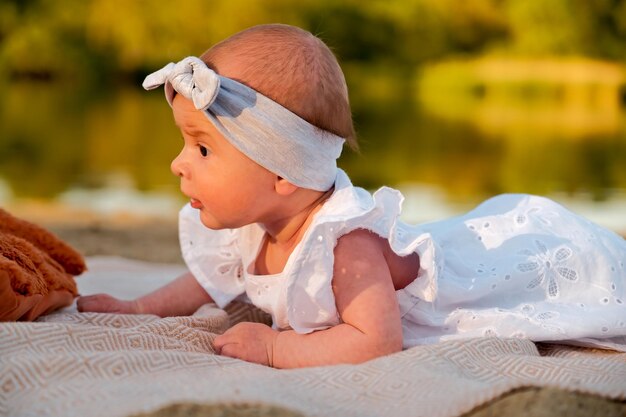 Newborn baby girl lies on the beach in a white dress