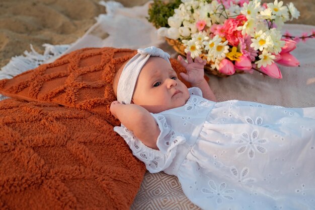 Newborn baby girl lies on the beach in a white dress