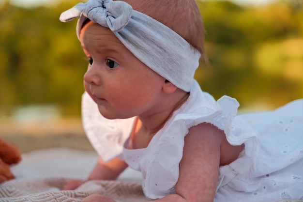 Newborn baby girl lies on the beach in a white dress