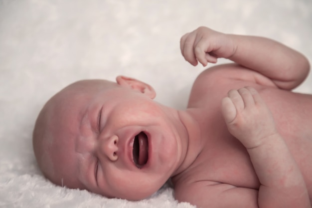 Newborn baby girl on light surface shows its emotions