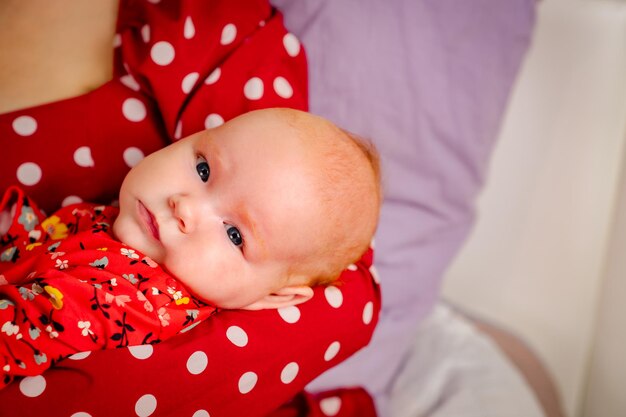 Newborn baby girl on mother's hands in red polka dot dress