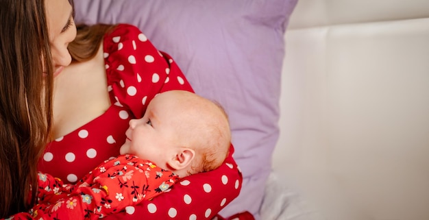 Newborn baby girl on mother's hands in red polka dot dress