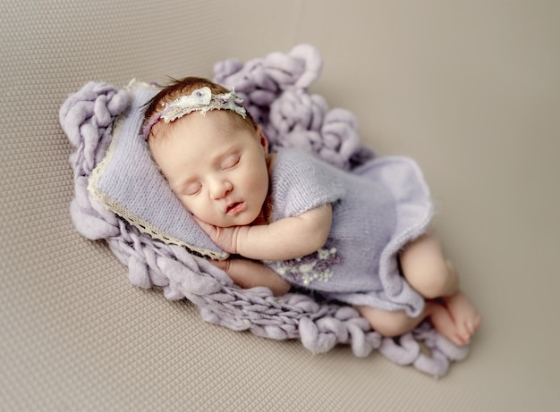 Newborn baby girl sleeping on knitted pillow and blanket Cute infant child kid napping and holding hands under cheek in studio