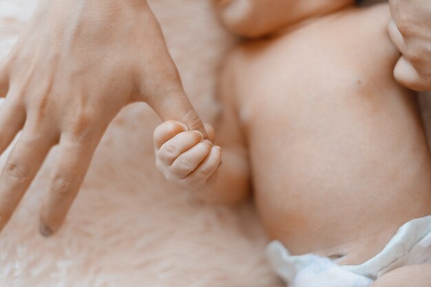 彼のお母さんの指のクローズアップを保持している新生児
