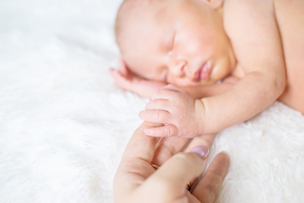 Новорожденный ребенок держит палец мамы