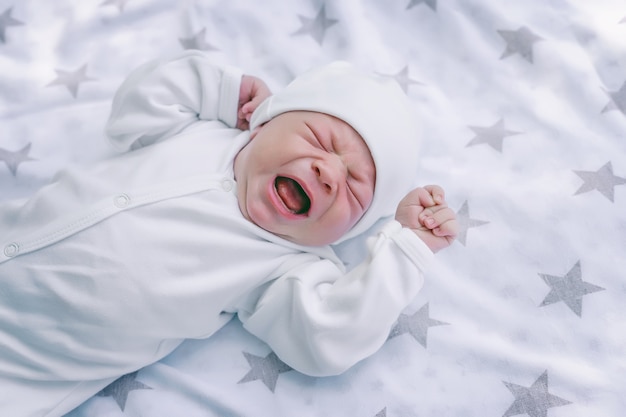 Newborn baby is lying in a crib screaming and crying