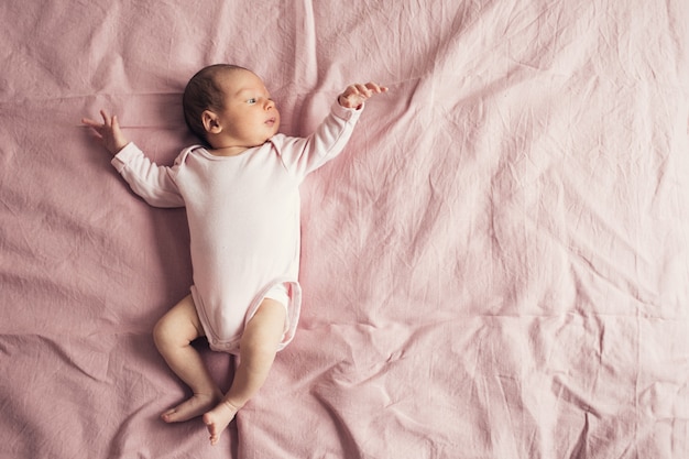 A newborn baby is lying on a pink background in a pink t-shirt